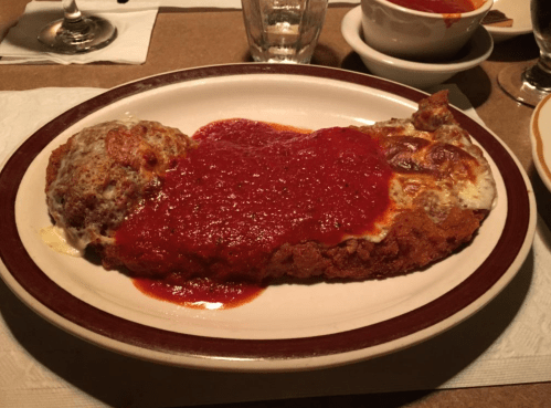 A plate of chicken parmesan topped with marinara sauce, served with a side of meatballs and melted cheese.