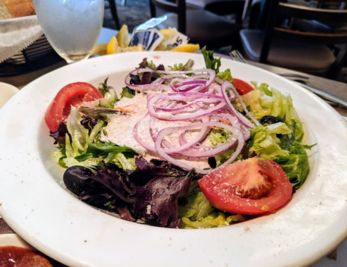 A fresh salad with mixed greens, sliced tomatoes, olives, and red onions, served on a white plate.