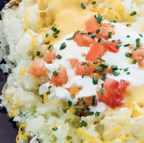 A close-up of a baked potato topped with melted cheese, sour cream, diced tomatoes, and chives.