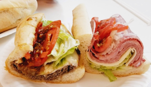 Two sandwiches on a plate: one with beef, cheese, lettuce, and tomato; the other with layers of deli meats and lettuce.