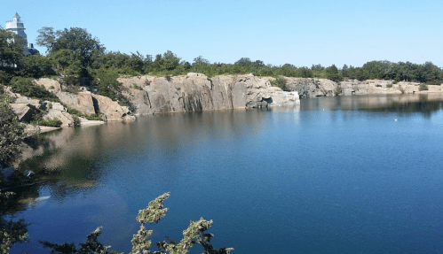 A serene lake surrounded by rocky cliffs and greenery under a clear blue sky.