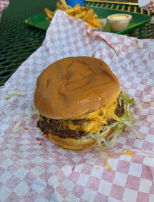 A cheeseburger with melted cheese and lettuce on a bun, served on a checkered paper with fries in the background.