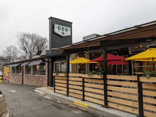 Exterior of a restaurant with a sign reading "BBB," featuring outdoor seating with colorful umbrellas.