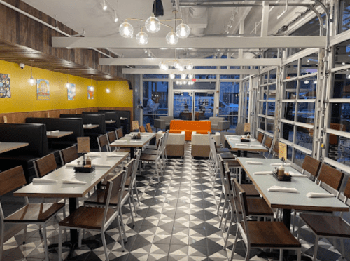 Modern restaurant interior with geometric tile flooring, wooden tables, and bright seating, featuring large windows.