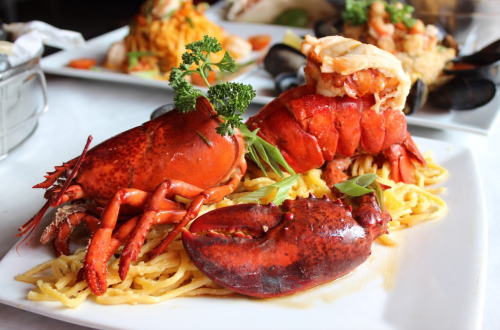 A plate featuring a whole lobster on a bed of pasta, garnished with parsley and green onions.