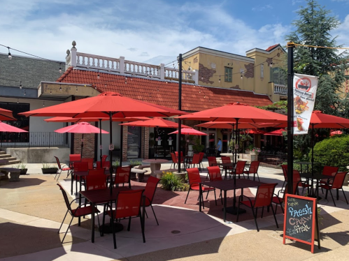 Outdoor dining area with red umbrellas and chairs, featuring a restaurant building in the background.
