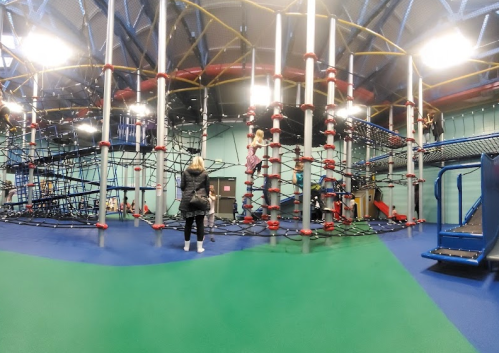 A colorful indoor playground with climbing structures and children playing, surrounded by safety mats.