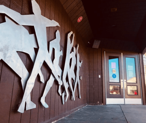 Metal silhouettes of people are mounted on a wooden wall beside a set of glass double doors.