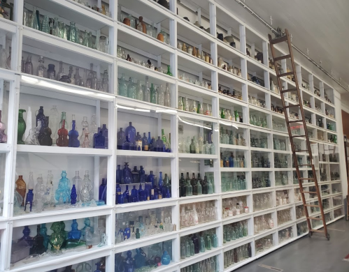 A wall of shelves filled with various glass lamps in different colors and styles, with a ladder leaning against it.
