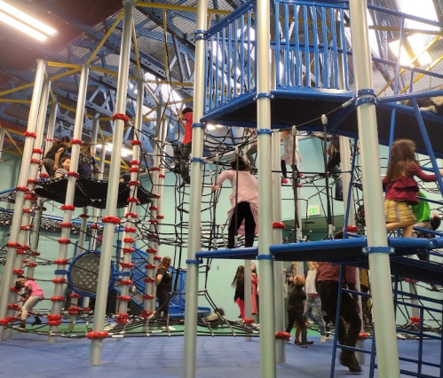 Children play on a colorful indoor climbing structure with nets and slides in a spacious play area.