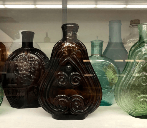 A collection of vintage glass bottles in various shapes and colors, displayed in a glass case.