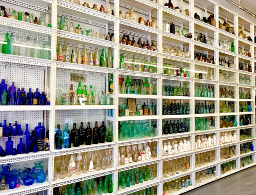 A wall of shelves filled with various colored glass bottles and jars, showcasing a diverse collection.