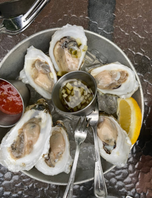 A platter of fresh oysters on ice, served with lemon, cocktail sauce, and a small cup of mignonette.