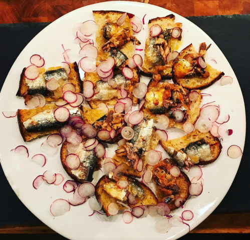 A plate of toasted bread topped with sardines and garnished with thinly sliced radishes.