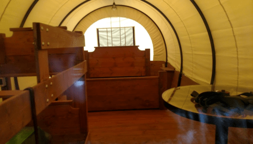 Interior of a tent with wooden furniture, including bunk beds and a round table, illuminated by soft light.