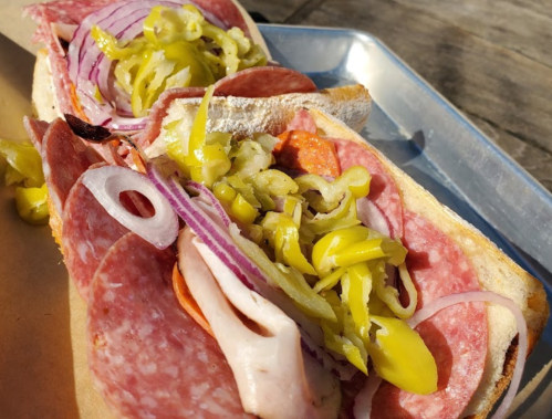 A close-up of a sandwich filled with various meats, onions, and pickled peppers on toasted bread.