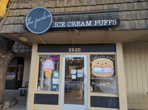 Exterior of "The Parlor" ice cream shop, featuring a sign and colorful window displays with ice cream and puffs.
