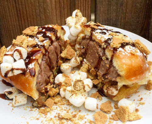 A split dessert featuring a doughnut filled with chocolate ice cream, topped with marshmallows, chocolate sauce, and crushed graham crackers.