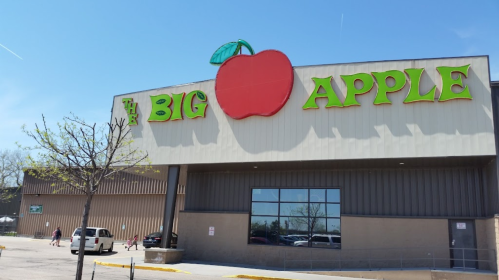 A large building with a sign reading "The Big Apple" featuring a red apple graphic on top. Clear blue sky in the background.