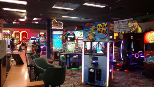 A vibrant arcade filled with colorful games and bright lights, featuring various machines and a lively atmosphere.