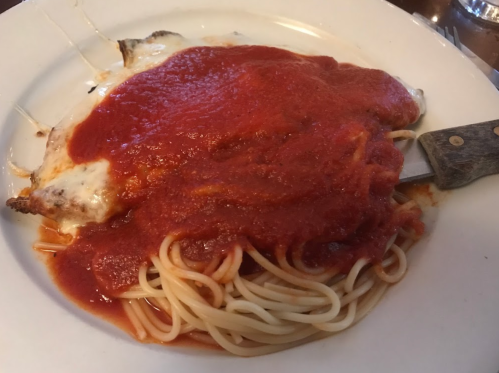 A plate of spaghetti topped with marinara sauce and a piece of baked fish covered in more sauce.