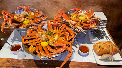 Three large bowls of seafood featuring crab, shrimp, and lemon, accompanied by sauces and bread on a wooden table.