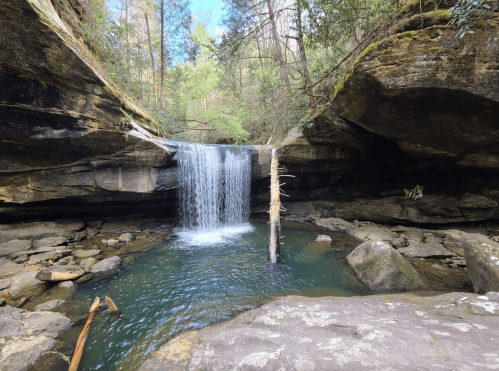 A serene waterfall cascades into a clear pool, surrounded by rocky cliffs and lush greenery.