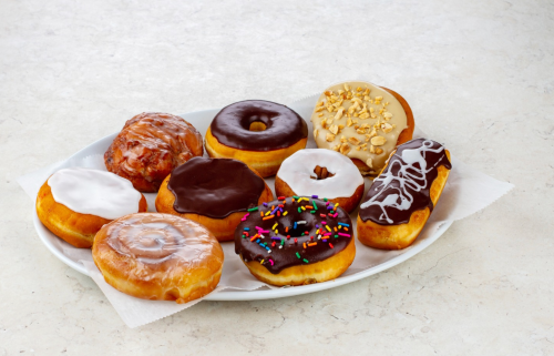 A platter of assorted donuts, including glazed, chocolate, and sprinkled varieties, on a light background.