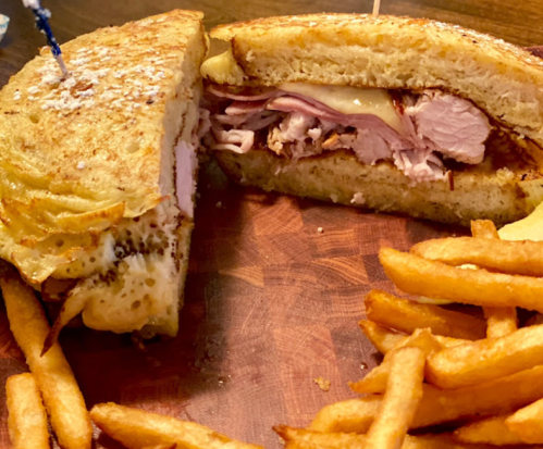 A close-up of a sandwich filled with turkey and cheese, served with a side of golden fries on a wooden board.