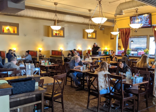 A busy restaurant interior with diners at tables, warm lighting, and a server attending to customers.