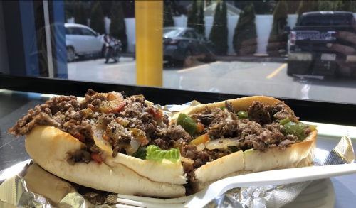 A close-up of a loaded sandwich with beef, vegetables, and cheese, served on a soft hoagie roll.