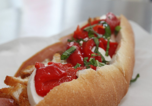 A close-up of a sandwich filled with fried chicken, mozzarella, ketchup, and fresh basil in a soft hoagie roll.
