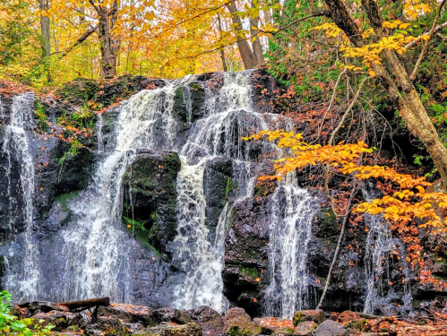 A cascading waterfall surrounded by vibrant autumn foliage and rocky terrain.
