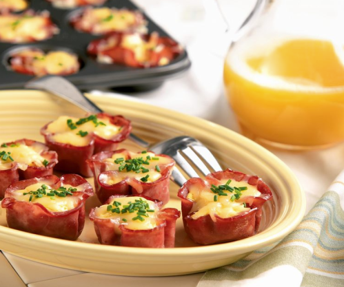 A plate of mini ham and cheese cups garnished with chives, alongside a glass of orange juice.