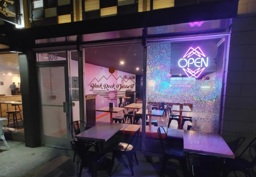 Exterior view of Black Rock Dessert shop at night, featuring an "OPEN" neon sign and tables outside.