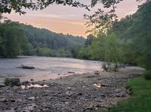 A serene river scene at sunset, surrounded by lush greenery and rocky shores.