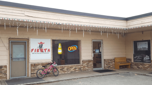 Exterior of Fiesta Mexican Restaurant with an "Open" sign, a bike outside, and festive lights hanging.