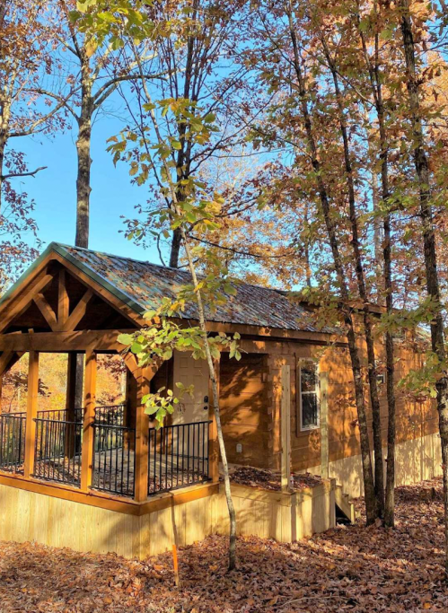 A cozy wooden cabin surrounded by autumn trees with colorful leaves and a clear blue sky.