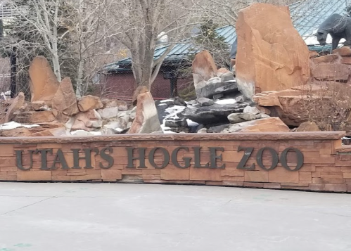 Sign for Utah's Hogle Zoo, featuring stonework and a natural landscape backdrop.