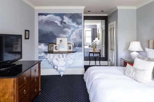 A stylish bedroom featuring a cloud mural, a wooden dresser, and a view of a bright, airy space beyond.