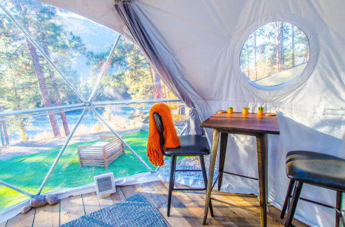 Cozy interior of a geodesic dome with a table, chairs, and a view of nature through large windows.