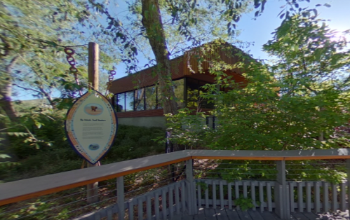 A modern building surrounded by greenery, with an informational sign in the foreground.