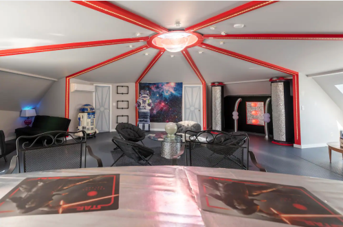 A themed room with red accents, featuring Star Wars decor, R2-D2, and a galaxy backdrop. Modern seating and lighting.