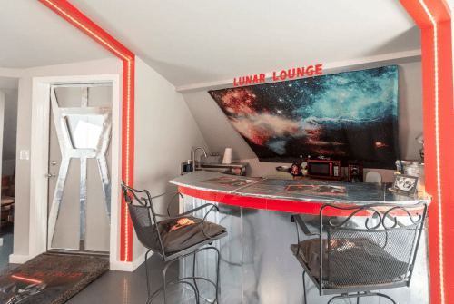 A cozy bar area with a cosmic-themed backdrop, featuring a sign that reads "Lunar Lounge" and modern seating.