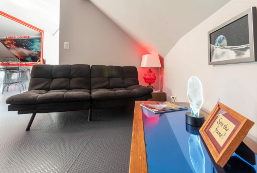 A modern living space featuring a black couch, a red lamp, and a blue table with decorative items.
