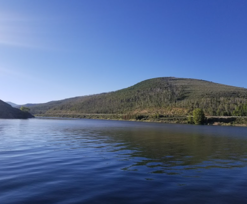 A serene lake surrounded by green hills under a clear blue sky.