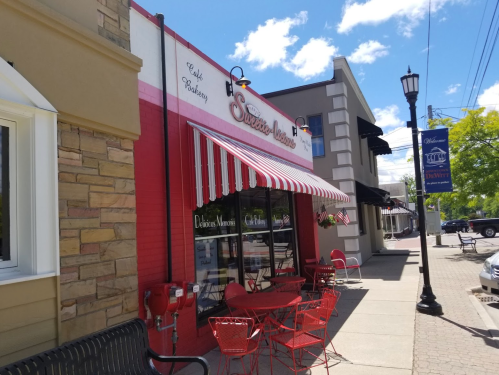 A charming bakery with a red and white striped awning, outdoor seating, and a welcoming storefront on a sunny day.