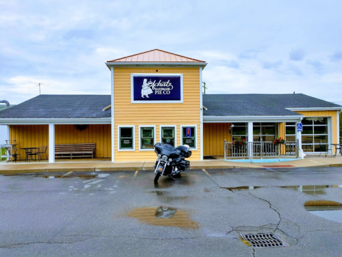 A yellow building with a sign for "Schatz Pie Co" and a motorcycle parked in front, under a cloudy sky.