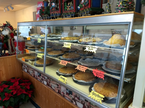 A display case filled with various pies, labeled with colorful tags, in a festive bakery setting.
