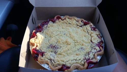 A freshly baked pie with a crumbly topping, sitting in a cardboard box inside a car.